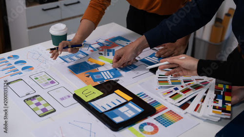 Foto Team of coworkers reviewing printed design mockups and charts on a table in an office, collaborating on branding or marketing strategy with coffee cups and stationery