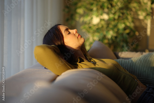 Woman is relaxing at sunset sitting on a sofa at home
