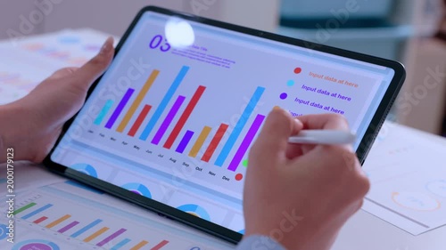 Focused professional person holding digital tablet and stylus analyzing colorful bar chart data on screen reviewing corporate financial report graph for business investment strategy growth
