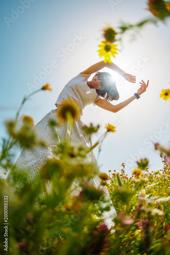 Summer mood. a young and cheerful girl posing against a background of blue sky and flowers. Happy girl among flowers and spring nature relaxing outdoors.