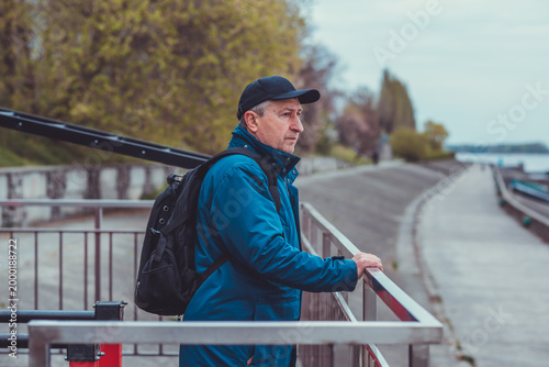 Thoughtful Mature Man with Backpack Looking at River. Active Lifestyle and Travel Concept