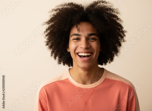 Joyful young man laughing openly in a studio portrait for youth lifestyle, diverse fashion marketing and modern skincare advertising against a neutral background