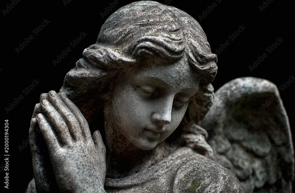 Obraz premium A serene angel statue with delicate features and folded hands, exuding tranquility against a dark background.