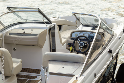 Open cockpit of contemporary motorboat featuring steering console, gauges, and cushioned seating, creating a clean scene of leisure navigation and relaxed water travel. Calm water and open windshield 
