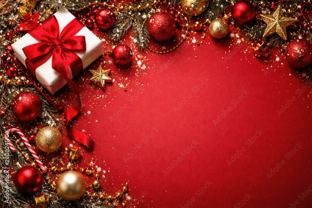 Fototapeta premium Decorative Christmas banner flat lay of red ribbon wrapped gift box with assorted red and gold baubles on red festive background with copy space