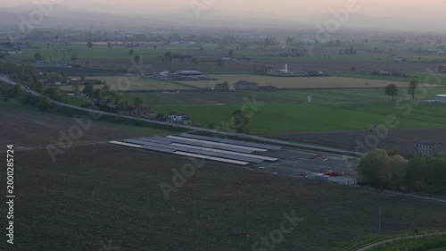 Aerial view of a solar energy farm under construction in the Po Valley at sunset, with agricultural fields and the SS9 Via Emilia road visible