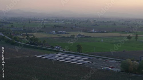 Aerial view of a large solar panel installation under construction in the Po Valley at dusk, with agricultural fields and distant mountains