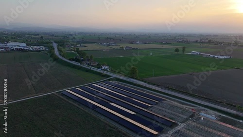 Expansive solar panel arrays under construction are visible alongside a highway in the Po Valley during a serene sunset