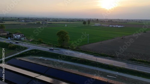 Aerial view of a solar farm under construction in the Po Valley at sunset, with the SS9 Via Emilia road visible and farmland surrounding the site