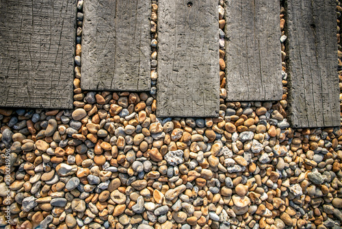 Vászonkép Rustic wooden planks arranged as a pathway through smooth mixed pebbles and river stones in natural beige, grey, and brown tones