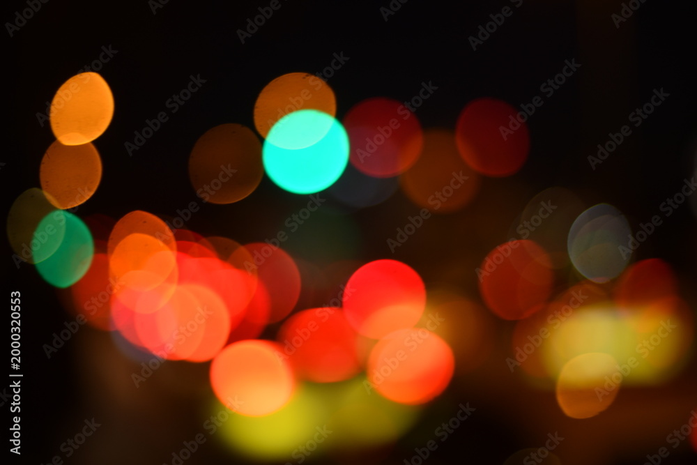 Fototapeta premium Abstract blurred city lights at night with colorful bokeh effect, featuring warm orange, red, green and yellow glowing circles. Ideal for urban nightlife themes, festive backgrounds, traffic concepts,
