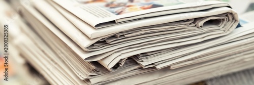A close-up of a neatly stacked pile of newspapers with visible text and images on the top sheets.