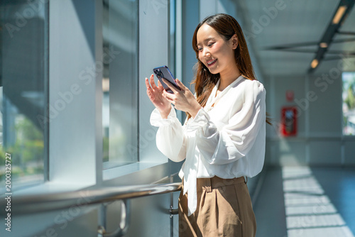 Foto Asian business traveler tapping on smartphone screen while standing in bright te