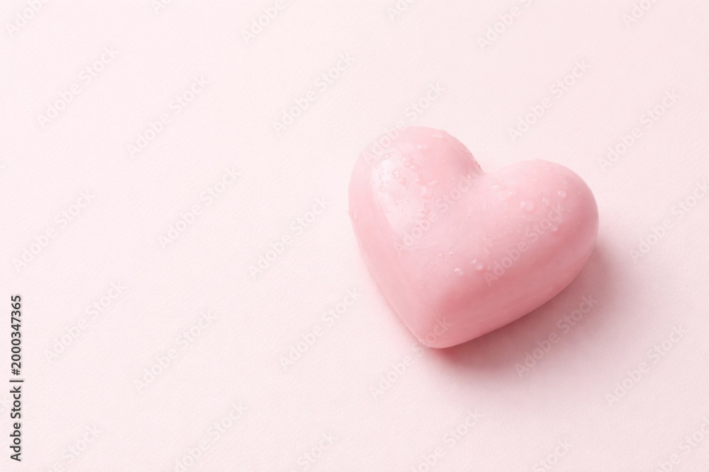 Fototapeta premium Heart shaped pink soap on a pale pink flat panel background with ample copy space