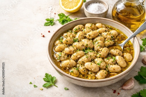 Bowl holding cracked cannellini beans drenched in herb flavored oil placed on a soft light backdrop including space for culinary text or copy