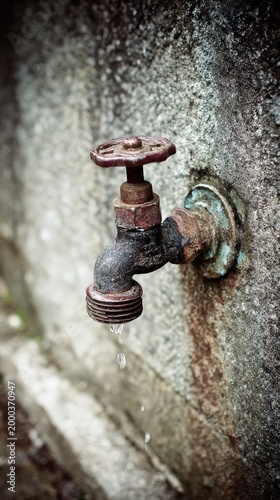 Rusty water faucet with dripping spout against a textured wall