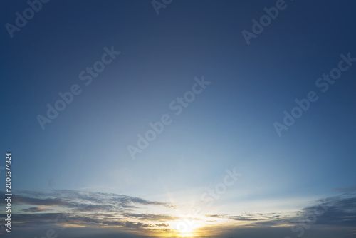 Fotografi A wide angle shot of a vibrant sunrise peeking through soft clouds on a deep blu