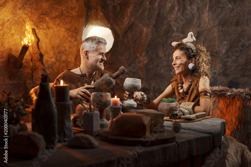 Romantic Caveman Couple Having Dinner Date – Galant Neanderthal Pouring Wine for a Happy Woman in a Cave Restaurant