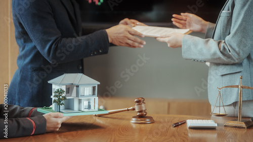 Fotografie Real estate contract signing with lawyer: hands exchanging documents over desk with model house, gavel and scales of justice, property sale or mortgage closing concept