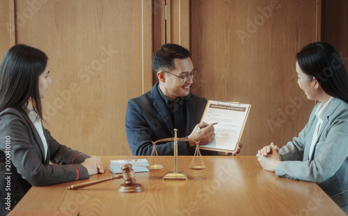 Businessman lawyer presenting contract agreement to two clients at meeting table with gavel and scales of justice in office, legal consultation concept.