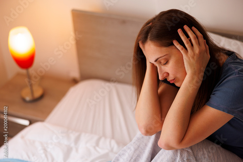 Depressed woman sitting in bed sad and tired after waking up