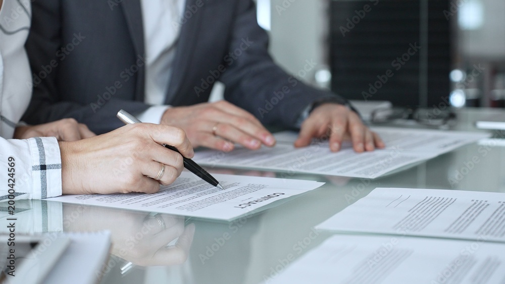 Fototapeta premium Group of professional business people sitting at a meeting table, reading and discussing contract terms, financial agreements. Collaboration, teamwork, and corporate communication concept
