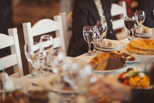 Waiters prepare tables for a wedding event with plates of food, glasses, and drinks. Guests are seated as the buffet is set with a variety of dishes and desserts