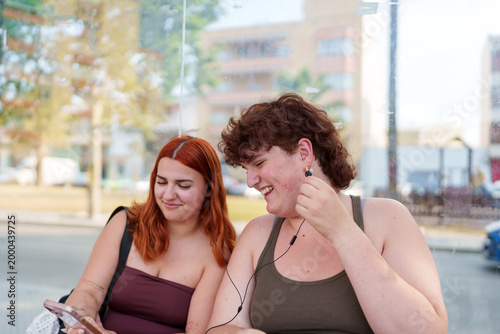 Photos Young women friends sharing wired earbuds and laughing, enjoying music and socia