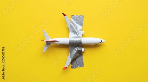 Toy airplane taped with duct tape on yellow background representing poor maintenance or budget travel.