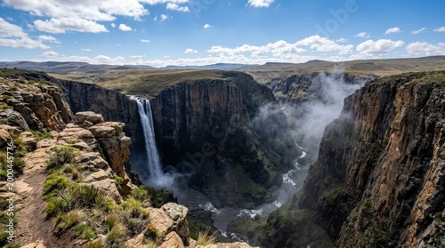 A dramatic precipice view of Maletsunyane Falls plunging from a rugged cliff, mist rising from the abyss, rocky plateau and vast open sky, crisp mountain light and awe-inspiring grandeur,