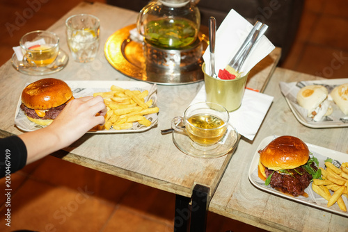 Canvastavla Young woman eating gourmet hamburger inside pub bar while drinking hot tea - Foo