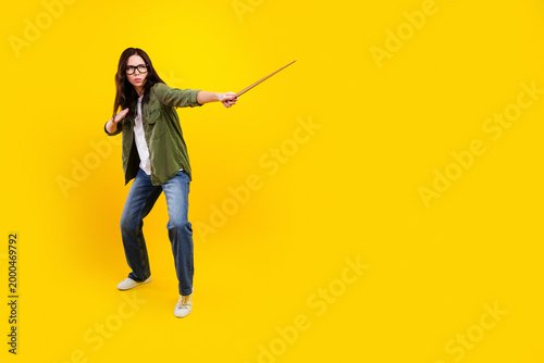 Billede på lærred Young woman in glasses striking a dynamic wizard pose with a wand on a vibrant y