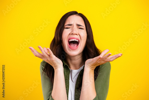 Fotografi Young woman screaming in frustration with hands raised on bright yellow backgrou