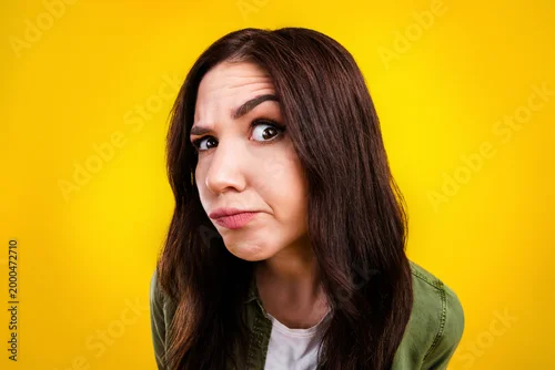 Fototapeta Skeptical young woman making doubtful face in a colorful studio portrait with yellow background