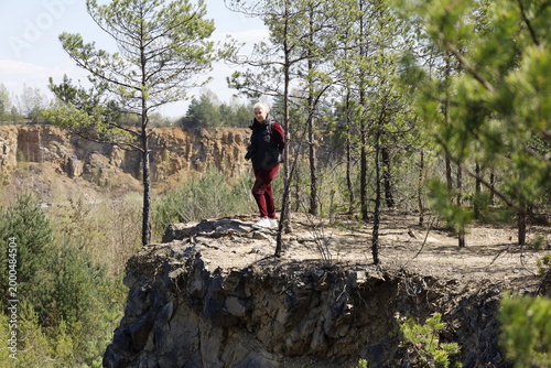 Woman with camera stands on a rocky cliff edge in a pine forest