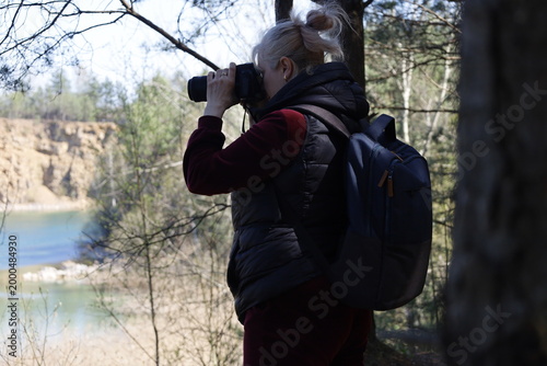 Woman with camera and backpack photographing a scenic quarry lake in the woods