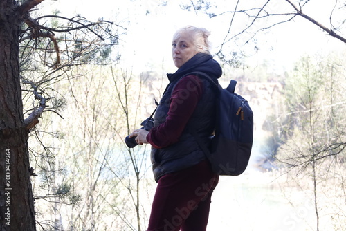 Woman with camera and backpack exploring a forest with a quarry in the background