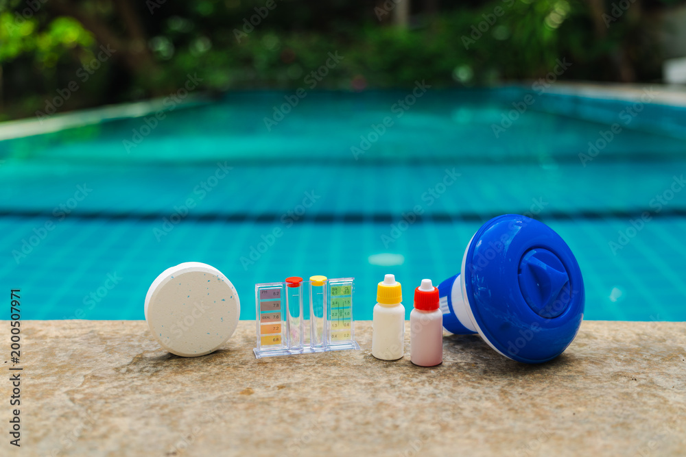 Obraz premium Pool maintenance tools lined on pool edge with chlorine tablet, water test kit, reagent bottles and floating dispenser