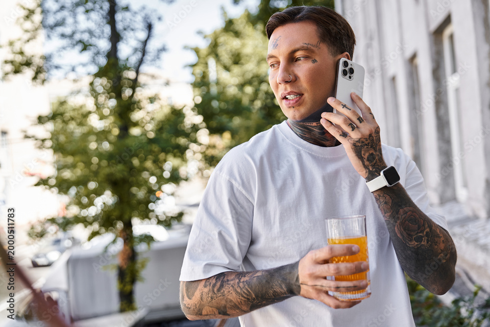 Fototapeta premium Young handsome man enjoying a refreshing drink at home while talking on the phone