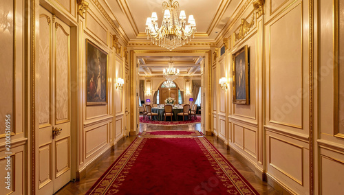 A grand hallway featuring red carpeting, chandeliers, and gold trim, leading to a banquet hall.