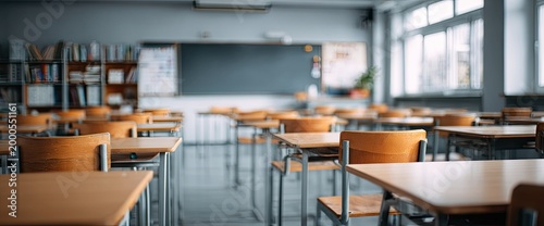 An empty classroom with rows of wooden desks and a chalkboard is shown in a soft focus.