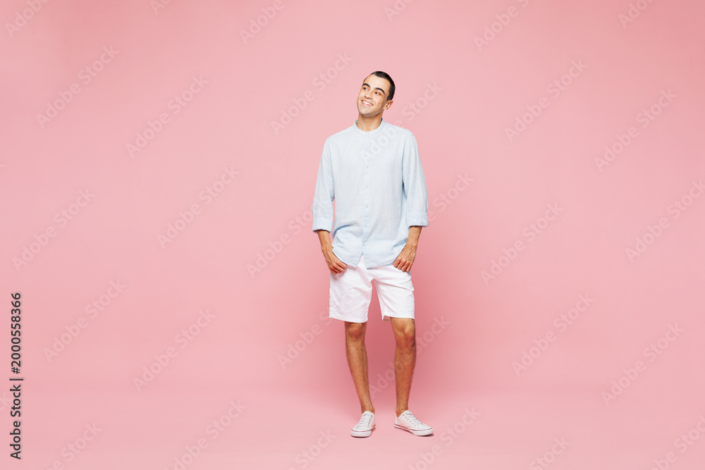 Fototapeta premium Full body smiling happy young middle eastern man he wear casual blue cotton shirt look aside on empty blank area isolated on plain pastel light pink wall background studio portrait. Lifestyle concept.