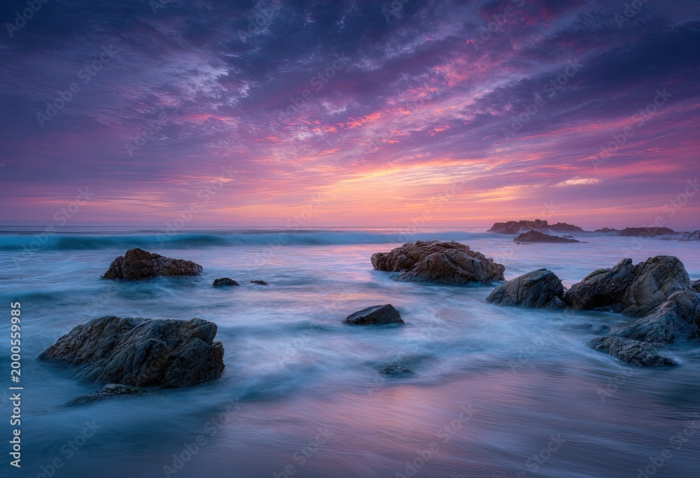 Obraz premium A vibrant sunset paints the sky with hues of pink and purple over a rocky coastline.