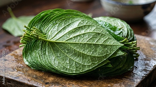 Stack of fresh green betel leaves with water droplets on rustic wooden cutting board.