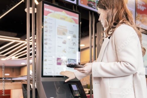 Konstfotografi Woman using self service kiosk with smartphone for contactless food ordering and