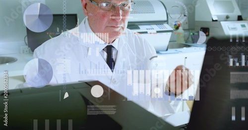 Viewing senior scientist reviewing monitors at lab bench, in lab coat, dark tie, glasses