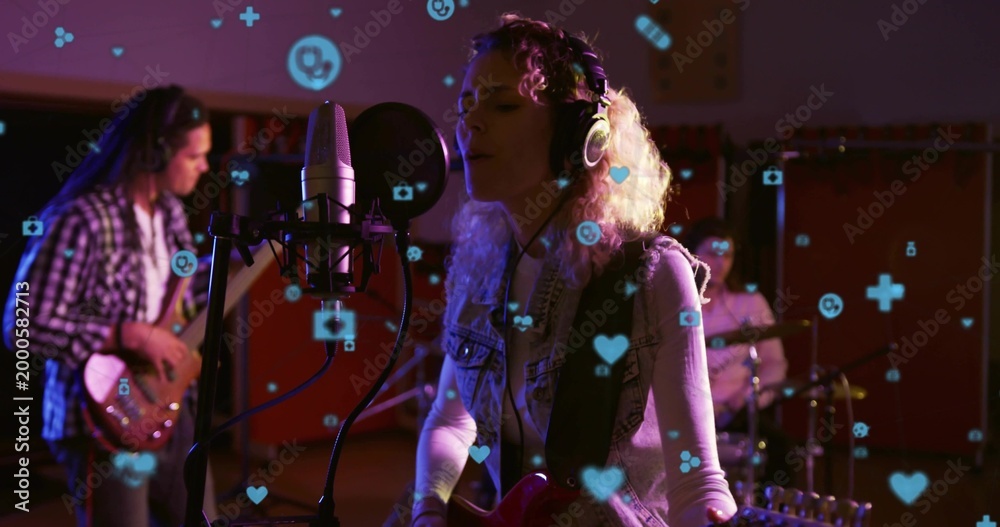 Fototapeta premium Singing singer wearing headphones holding guitar in dim studio with mic, pop filter, floating icons