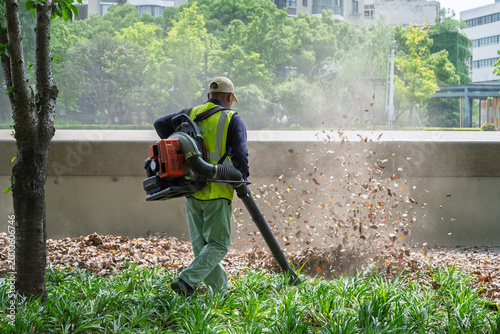 Fotografía Worker in High-Visibility Vest Using Backpack Leaf Blower in Urban Park