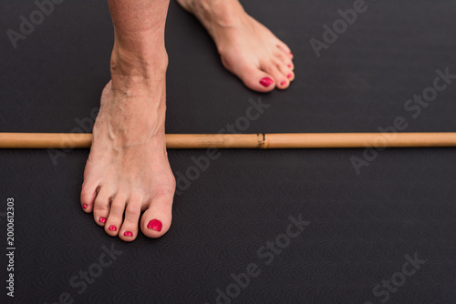 Female foot rolling a smooth wooden stick for foot deformation problem prevention. Bare feet rolling over a bamboo rod for foot therapy and arch stimulation