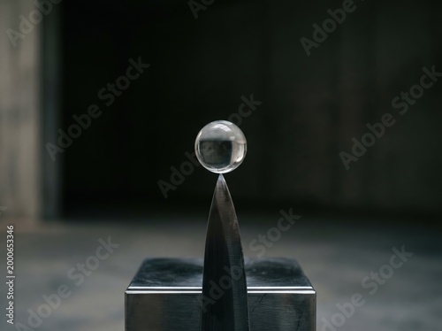 Clear glass sphere balanced on a metal tip for minimalist background and product composition with reflective material study for studio display